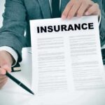 Health Costs Spike – Brace For 2027 Person in suit holding an insurance document and a pen