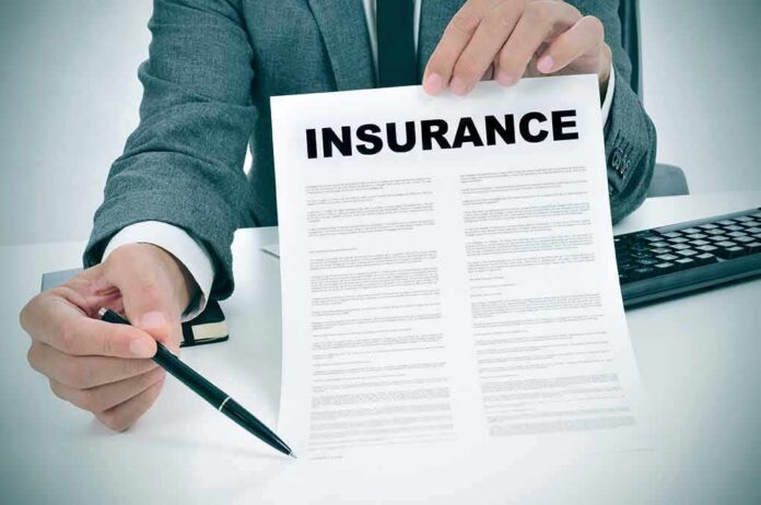 shutterstock_236845816 Person in suit holding an insurance document and a pen
