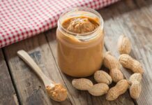 Jar of peanut butter with spoon and peanuts on rustic table