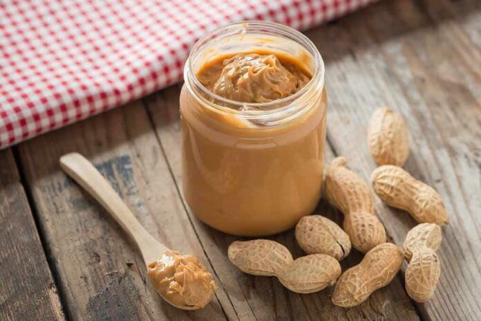 Jar of peanut butter with spoon and peanuts on rustic table