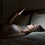 Woman lying in bed looking at smartphone