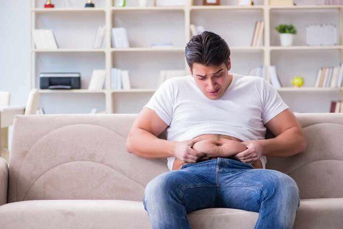 shutterstock_678496093 Manny MUA sitting on a couch pinching his belly
